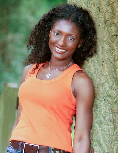 lady in an orange top leaning against a tree
