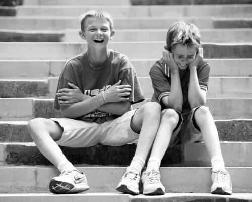 monochrome photo of 2 boys sitting on steps and sharing a joke