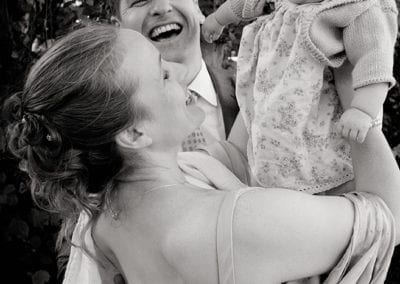 bride and groom laughing with baby on their wedding day