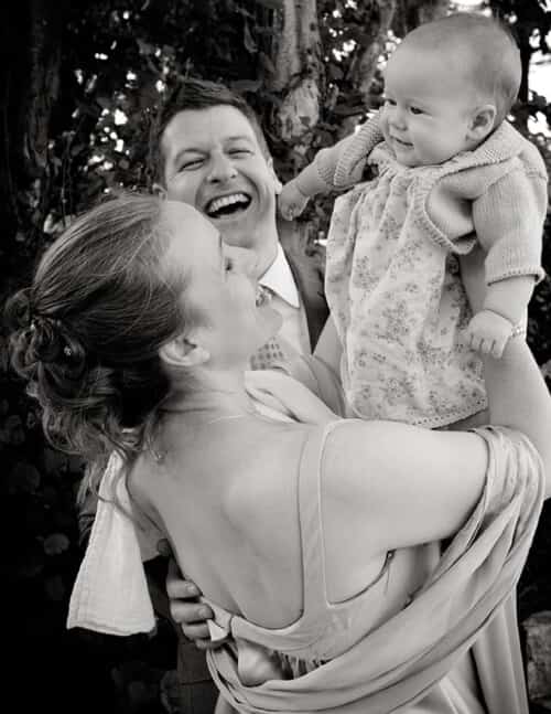 bride and groom laughing with baby on their wedding day